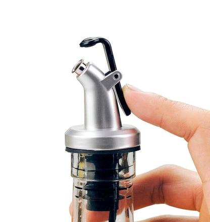 ELLORA FARMS silver chef pourer bottle spout with a black snap-on lid being operated by a hand for precise pouring.
