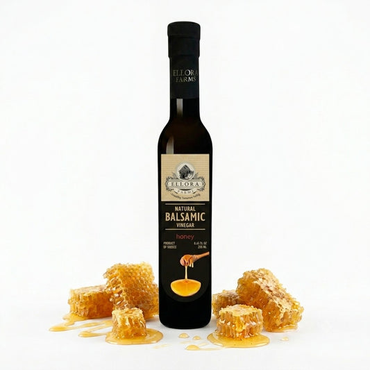 ELLORA FARMS honey infused balsamic vinegar bottle surrounded by fresh honeycomb pieces on a white background.